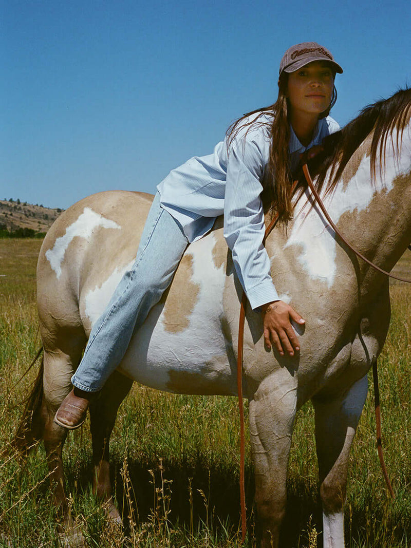 Cowgirl Jean worn while riding a horse in a scenic field, showcasing Western style and durability.