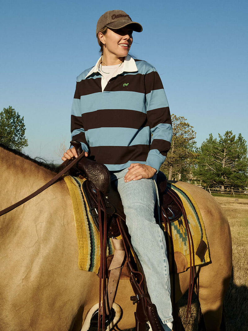 Woman wearing a Club Polo while riding a horse in a sunny field, showcasing the stylish design and vibrant colors.