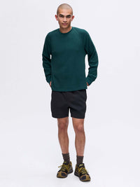 Model standing in green Waffle Longsleeve with relaxed fit, paired with black shorts for active wear.