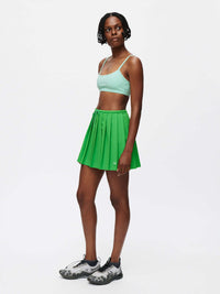 Model wearing a Solar Bra with a green pleated skirt, showcasing a sporty and stylish look for activewear.