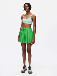 Model wearing the Stardust Skirt, a pleated skirt in green with side zipper and drawstring tie, showcasing lightweight fabric.
