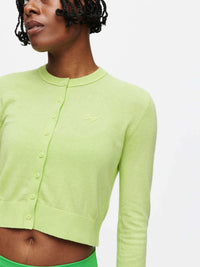 Model wearing a vibrant green Sugar Cardigan made of soft cotton cashmere, featuring hand-embroidered OV signature.