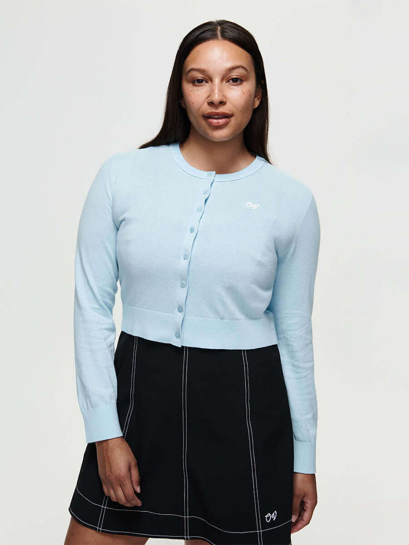 Model wearing a light blue Sugar Cardigan made of soft cotton cashmere, featuring hand-embroidered OV signature.