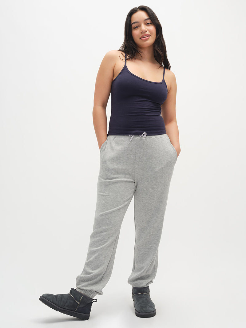 Woman wearing a navy tank top and gray sweatpants on a white background