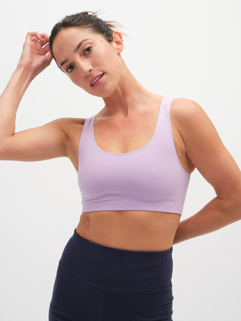 Woman wearing a light purple sports bra and dark blue leggings on a plain background