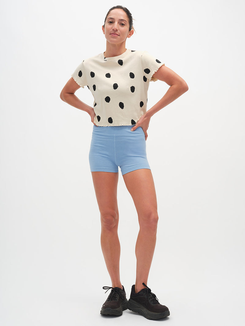 Woman wearing a polka dot shirt and light blue shorts on a white background