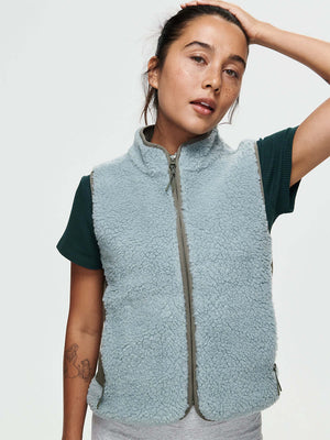Woman wearing a light blue CandyFleece Vest over a dark green shirt, styled for a casual look.