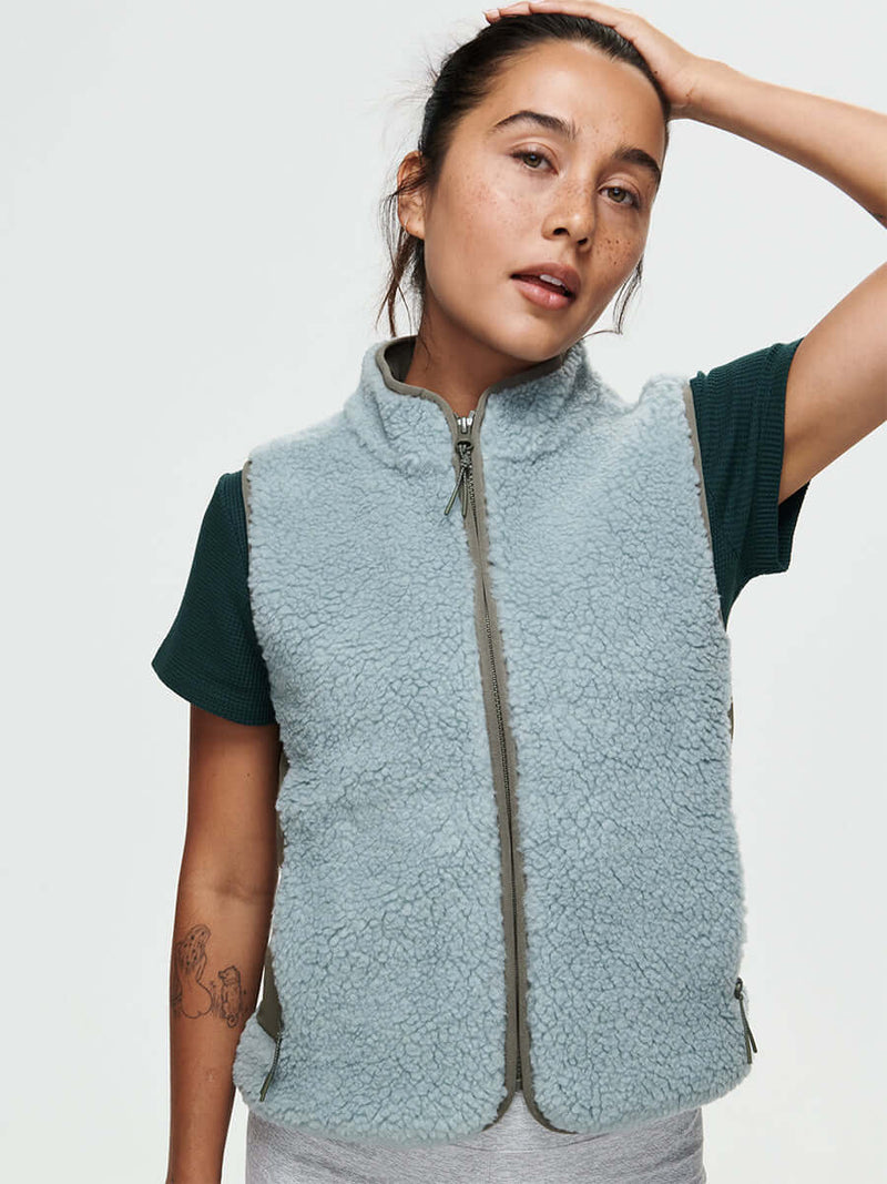 Woman wearing a light blue CandyFleece Vest over a dark green shirt, styled for a casual look.