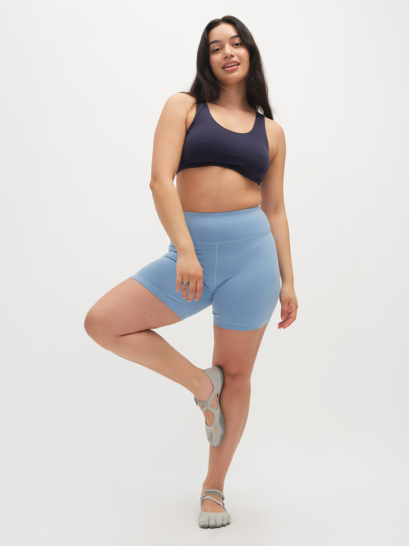 Woman wearing a navy blue sports bra and light blue shorts on a white background