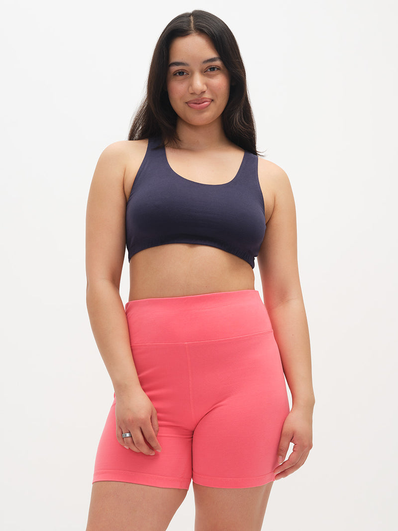 Woman wearing a dark blue sports bra and pink shorts on a white background