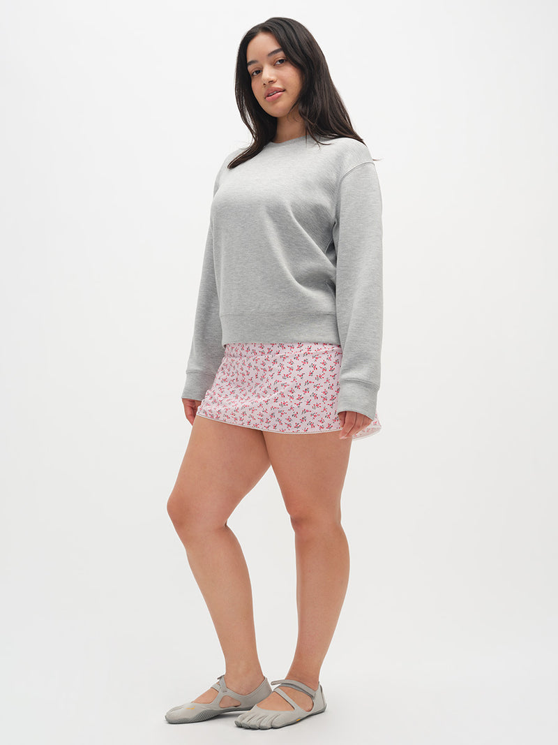 Woman wearing a gray sweater and pink skirt on a white background