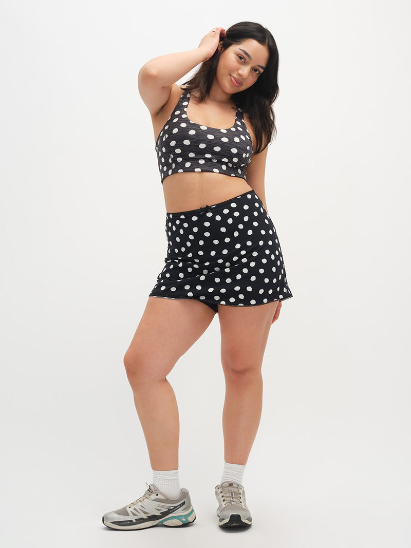 Woman wearing a black and white polka dot sports bra and shorts set on a white background
