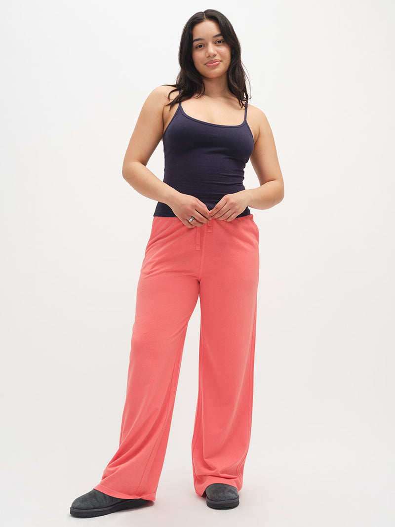 Woman wearing a navy tank top and coral pants on a white background