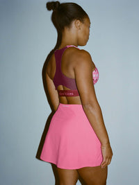 Person wearing a pink sports bra and skirt with visible branding on a plain background