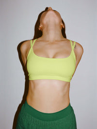 Model posing in Apple Bra in Neon Yellow with intersecting straps, styled for activewear.