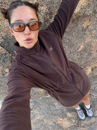 Model posing in Boulder Dress in Brown, featuring adjustable waist toggles and front zippered pockets.