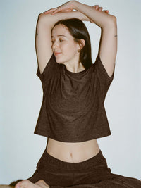 Model stretching in CloudKnit Boxy Shortsleeve in Dark Brown, showing cropped length and relaxed fit.