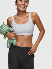 Model smiling while wearing CloudKnit Wide Leg Pant in Black with a soft grey crop top, holding a green checkered plush toy.
