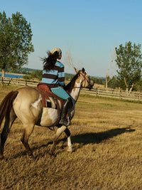 Woman wearing a Club Polo riding a horse in an open field during fall, with style and comfort.