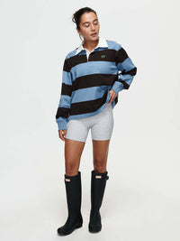 Model wearing a Club Polo with blue and black stripes, for fall layering, paired with shorts and rain boots.