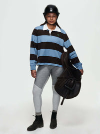 Model wearing a Club Polo, styled with grey leggings and a riding helmet, holding a saddle, for fall layering.