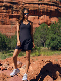 Model standing in a rocky landscape wearing Doing Things Dress in Black, with sporty design and breathable fabric.