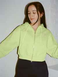 Model posing in The Diamanté Doing Things Hoodie in bright green, featuring diamante script and a cropped design.