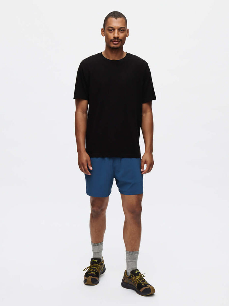 Model standing in Everyday Classic Shortsleeve in Black, paired with blue shorts for active recreation.