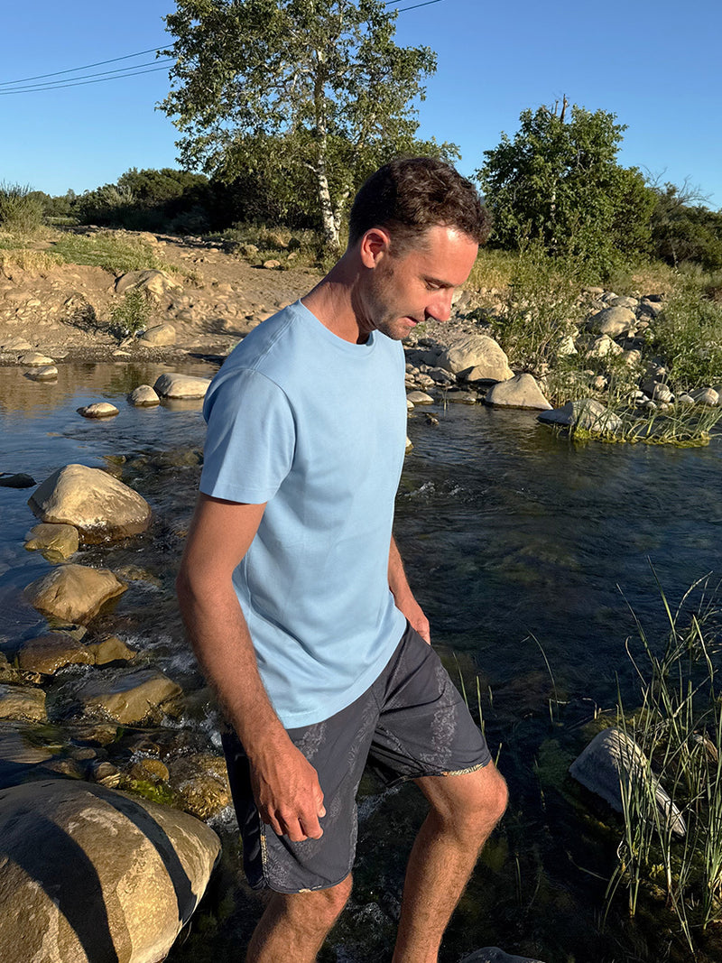 Man walking on stones by a stream wearing Everyday Classic Shortsleeve in Light Blue, soft organic cotton jersey.