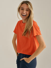 Model smiling while wearing Everyday Shortsleeve in Orange, featuring a relaxed fit and slight crop.