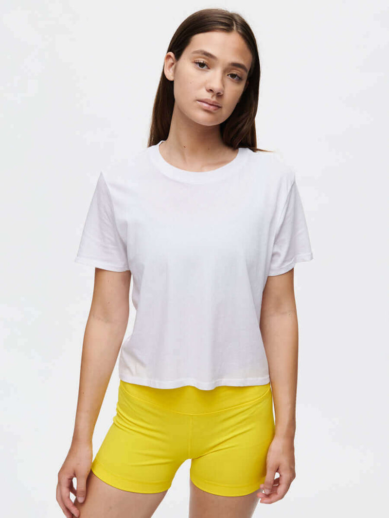 Model standing in relaxed pose wearing Everyday Shortsleeve in White, slightly cropped fit paired with yellow shorts.