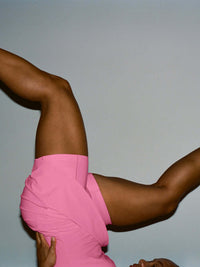 Model in a playful pose wearing The Exercise Dress in Pink, featuring a built-in shorts liner.