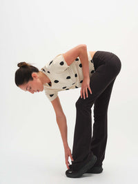 Model bending to tie shoes while wearing Flared Legging in Cotton Candy, featuring an extra-tall waistband for custom fit.