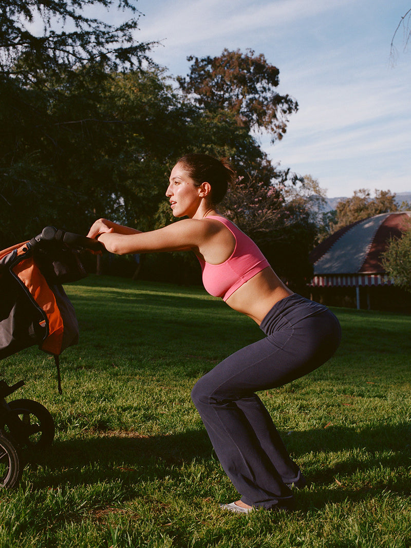 Model performing a squat in a park wearing Double Dip Bra in Cotton Candy, with wide shoulder straps for support.