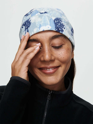 Model smiling and wearing Frosted Beanie with exclusive Elf Garden print, cozy fleece fabric.