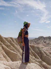 Person standing on rocky terrain wearing a black crop top and wide-leg pants, styled for hiking.