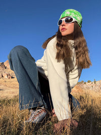 Model kneeling in field wearing Frosted Beanie with Elf Garden print, cozy fleece fabric for warmth.