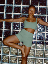 Model in a yoga pose wearing Gemini High Rise Short in Soft Green, featuring a wide waistband and smooth texture.