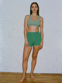 Model wearing Gemini High Rise Short in Green with a wide waistband for added support.