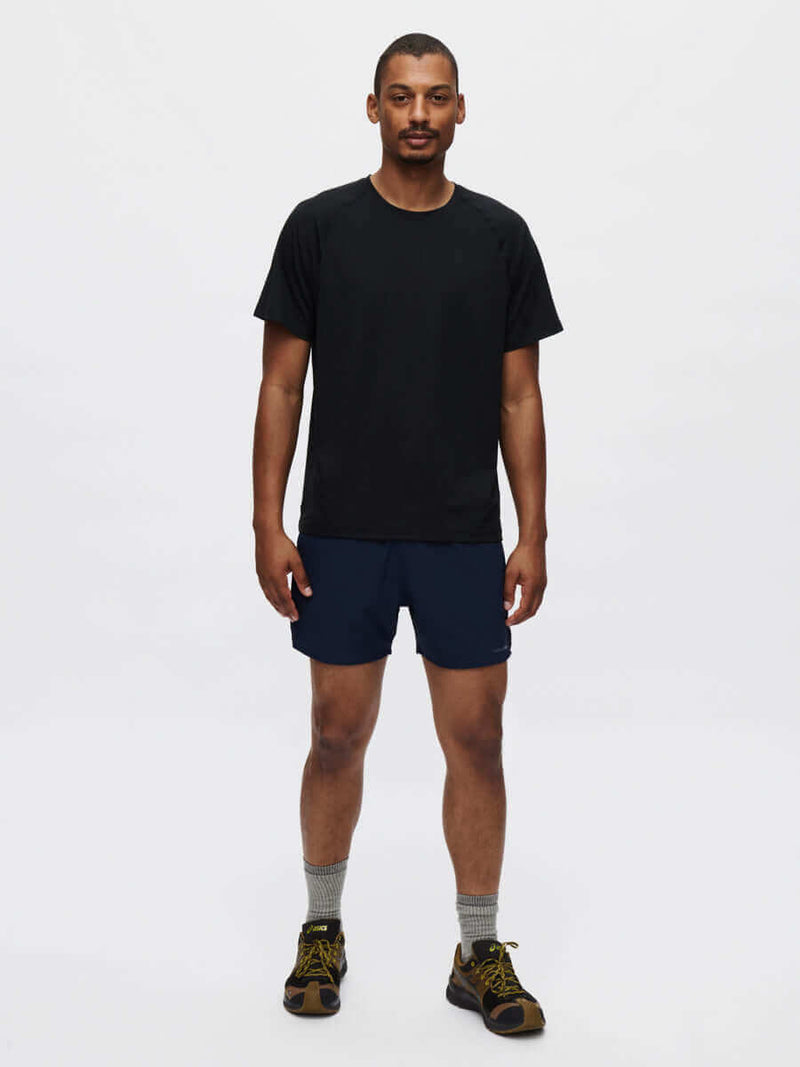Model standing in black tee and High Stride 5" Short with Pockets in Navy, featuring side pockets for convenience.