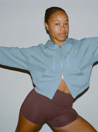 Model posing in The Diamanté Doing Things Hoodie, blue with diamante script and cropped length.