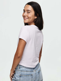 Smiling model wearing the Mustang Tee in Orchid Dust from the back, with soft cotton fabric and casual style.