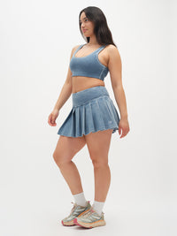 Model in a side pose wearing Orbit Bra in Blue, paired with a matching denim pleated skirt.