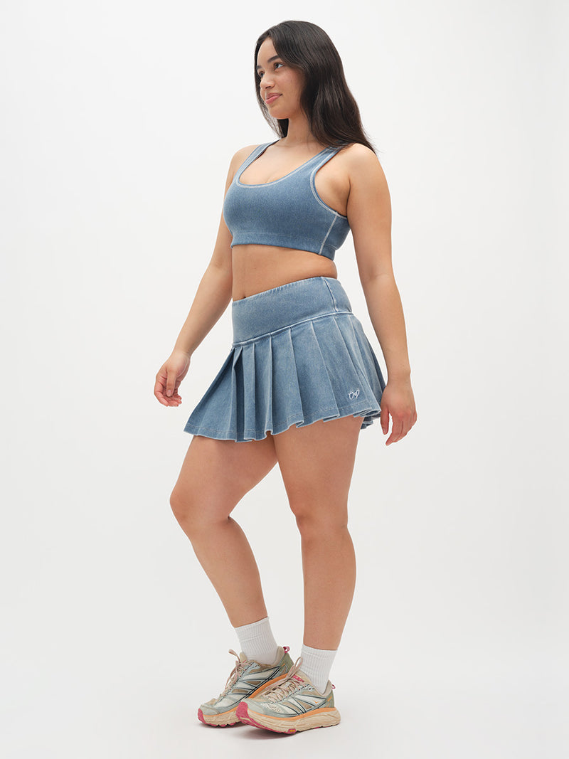 Model in a side pose wearing Orbit Bra in Blue, paired with a matching denim pleated skirt.