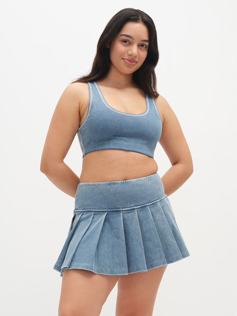 Model posing in denim Orbit Bra, featuring a soft fit and paired with a matching pleated skirt.