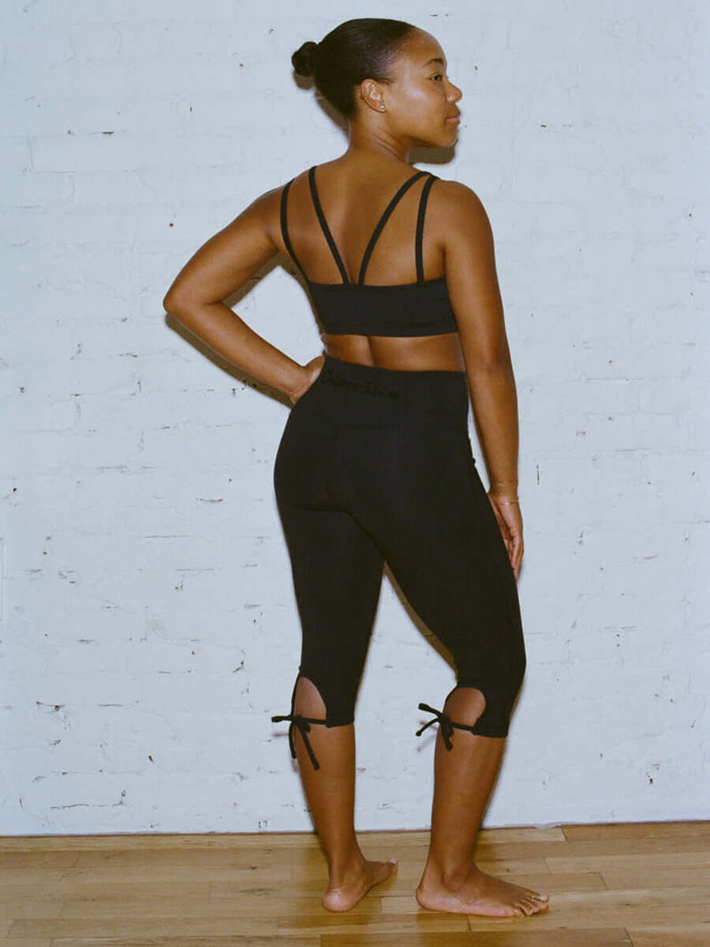 Side view of model wearing Puddle Capri in Black, featuring keyhole cut-outs and adjustable ties.