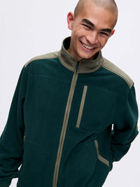 Model smiling in RecFleece Relaxed Full Zip in Dark Green, featuring contrast shoulder panels and pockets.
