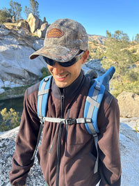 Man smiling while hiking, wearing RecFleece Relaxed Full Zip jacket in Black, with adjustable straps on his backpack.