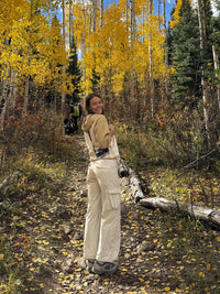 Model posing in a forest wearing RecTrek Cargo Pant in Cream, featuring utility pockets and a relaxed fit.