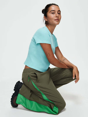 Model kneeling in RecTrek Zip Pant in Olive with mesh panel zippers for ventilation.